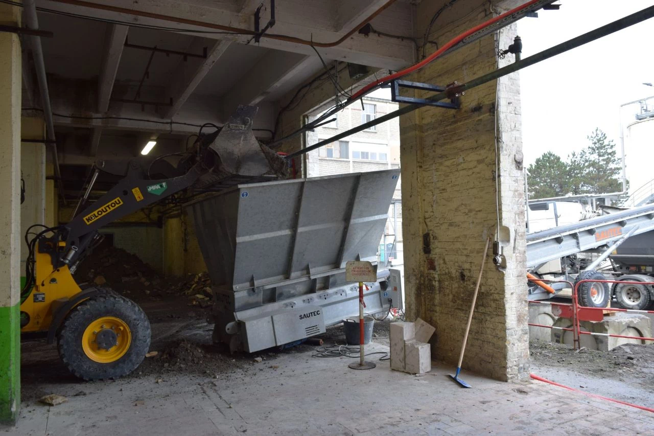 Une chargeuse alimente au godet un tapis transporteur pour évacuer les gravats d'un chantier.